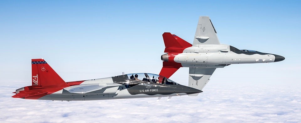 Two T-7A Red Hawk jets flying in formation above the clouds